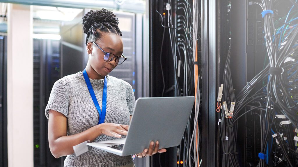 Shot of a young woman using a laptop in a server room